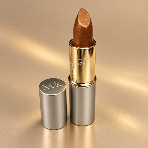 Mary Kay Gold Dust golden bronze lipstick on a warm champagne background