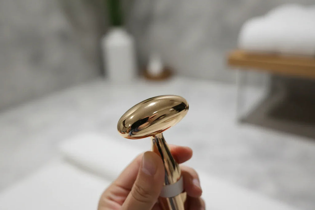 In-hand close-up of the Galahome gold-plated sonic facial massager head with shallow depth of field