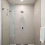 American Standard Studio S chrome pressure balance trim in a contemporary walk-in shower with beige porcelain tile and matching chrome shower head.