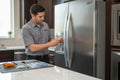 Appliance technician repairing a stainless steel refrigerator water and ice dispenser assembly in a modern kitchen