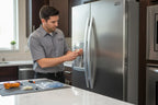 Appliance technician repairing a stainless steel refrigerator water and ice dispenser assembly in a modern kitchen