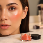 Close-up of woman's glowing dewy cheeks with tangerine flush and Mary Kay Cheek Glaze jar visible on vanity in foreground