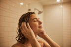 Woman with wavy curly hair applying conditioner in shower fingers working through wet textured hair lifestyle photo