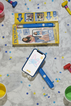 Pictionary Air 2 game set up with phone on stand showing air drawings, blue pen beside yellow game box — More4less Outlet