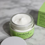 Close-up macro detail of Cocokind Texture Smoothing Cream jar showing smooth cream texture with green label, shallow depth of field