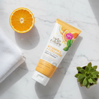 Morning skincare routine flat lay with cleanser tube, white towel, orange slice, and small green plant on marble vanity