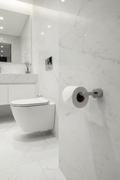 Grohe Atrio SuperSteel matte toilet paper holder with toilet paper roll mounted on white marble bathroom wall next to modern toilet