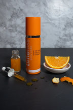 Modern minimalist lifestyle photograph of Vitamin C skincare essentials including an orange serum bottle on dark slate surface