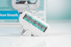 Water droplets splashing over teal Gillette Venus Deluxe Smooth Sensitive 5-blade razor cartridge with SkinElixir lubrication strip on white surface