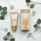 Overhead flat lay of Jergens Natural Glow gold gradual tanning face lotion tube and box beside fresh botanicals on white marble