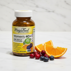 MegaFood Women's 40+ One Daily amber glass bottle beside fresh organic oranges cranberries and blueberries on white marble – More4less Outlet
