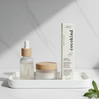 Modern minimalist vanity arrangement featuring Cocokind Retinol Gel white box beside glass dropper bottle and small jar, soft diffused light