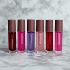 Macro close-up six Manna Kadar pH lip oil bottles vibrant translucent colors red pink purple — More4less Outlet