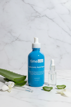 Professional minimal arrangement of botanical skincare ingredients next to a large blue glass serum bottle on white marble