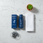 Minimalist men's morning skin routine flat lay with navy blue lotion bottle and white linen towel on marble