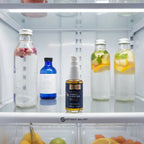 Quicksilver Scientific Liposomal Vitamin C pump bottle inside stainless steel refrigerator door shelf next to premium botanical waters signifying refrigeration requirement