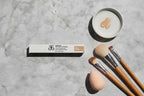 Arbonne The Real Conceal Liquid Concealer Tan flat lay on slate surface with blending brushes