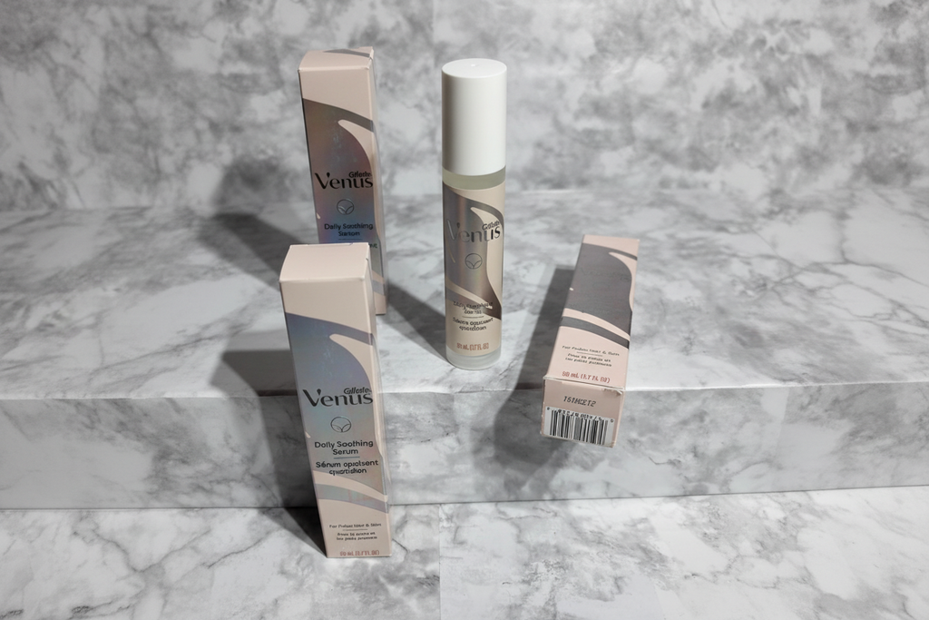 Professional flatlay of three Gillette Venus Daily Soothing Serum bottles with retail cartons on white marble in bright natural daylight