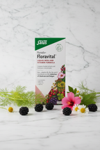 Salus Floradix Floravital Liquid Iron and Vitamin Formula 500ml retail box on white marble with green and red botanical props, blackberries, fennel, hibiscus and chamomile flowers, minimalist studio photography – More4less Outlet