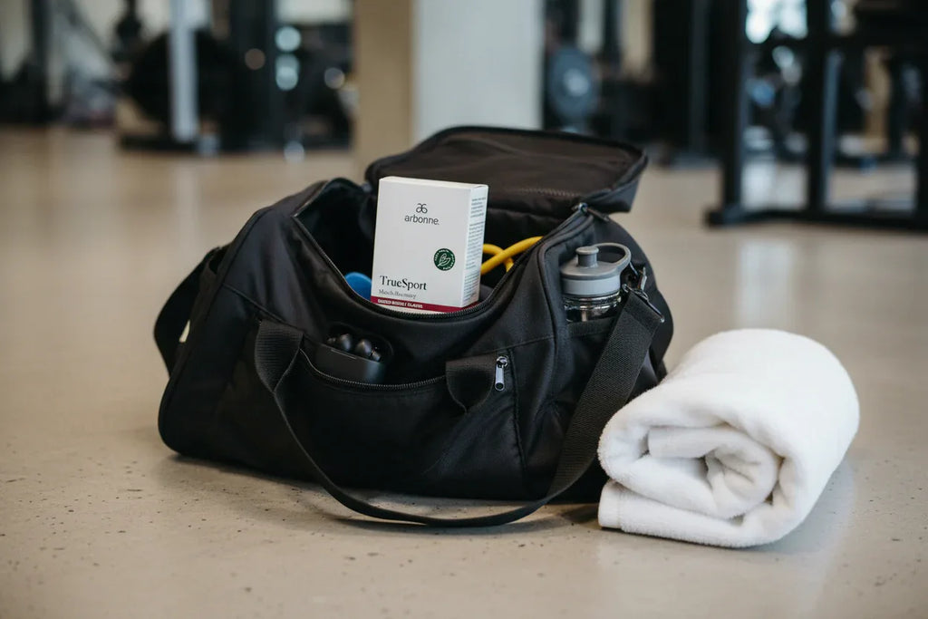 Arbonne TrueSport Muscle Recovery box in gym bag setup on neutral surface with folded towel