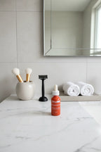 Modern professional bathroom setup with curated minimal health and beauty supplies including a small dark amber glass serum bottle on white marble
