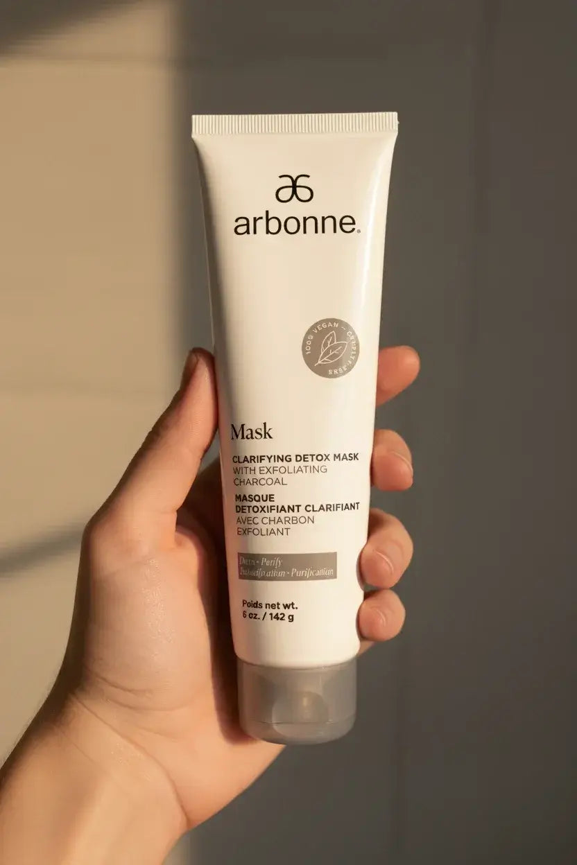 Hand holding Arbonne Clarifying Detox Mask with Exfoliating Charcoal tube in warm sunlight - More4less Outlet