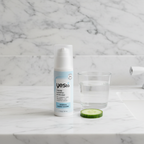 Yes To Intense Hydration Moisturizer pump bottle on marble counter with cucumber slice and glass of water.