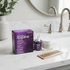 Women's Rogaine 3-Month Supply box on white quartz bathroom vanity with wide-tooth comb and skincare jar