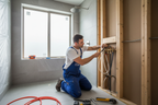 Professional master plumber installing a shower valve rough-in inside a bathroom wall