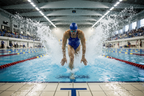 Competitive swimmer pushing off pool wall wearing blue swim goggles, indoor Olympic pool
