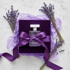 Lifestyle — purple perfume bottle in gift box with deep violet ribbon, dried lavender sprigs, and purple tissue paper on white marble — editorial for visual context only