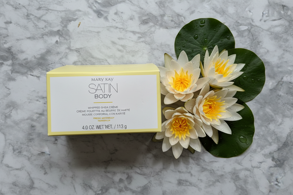 Yellow luxury body cream box next to fresh white waterlilies on marble surface