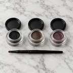 Mary Kay Gel Eyeliner in Jet Black, Espresso Ink and Ornate Orchid with brush on a marble vanity