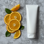 Vibrant fresh orange slices and green leaves beside minimalist white skincare tube on clean marble surface