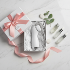Lifestyle — white electric facial brush in gift box with white tissue paper, pink ribbon bow, and small skincare bottles on marble — gifting flatlay editorial for visual context only