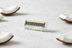 Close up of a women's razor cartridge refill on clean white bathroom marble with coconut accents