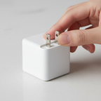 Close-up hands folding AC prongs into sleek white square power adapter on clean surface
