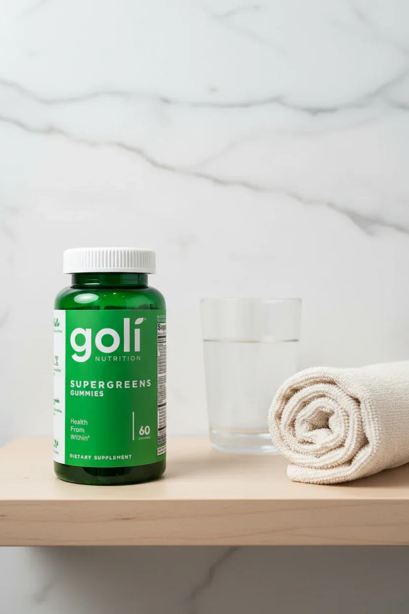Goli Supergreens Gummies jar on minimalist bathroom vanity shelf with rolled cotton towel and glass of water — More4less Outlet