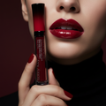 Woman with bold glossy red lips holding Mary Kay Vinyl Lip Shine tube in dramatic editorial beauty lighting
