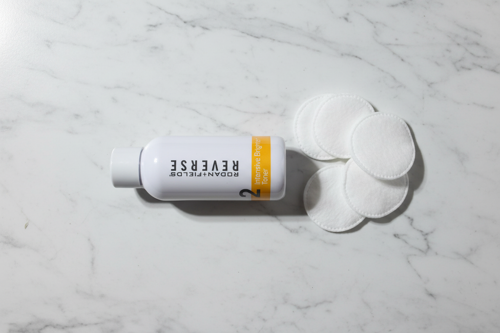 Rodan + Fields REVERSE Intensive Brightening Toner in minimalist spa flat lay with cotton pads on marble
