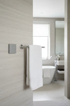Legrand Adorne magnesium paddle switch installed on light-grey stone bathroom wall next to chrome towel bar