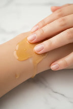 Close-up of clear golden argan oil being worked into smooth skin on a white marble background