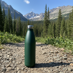 Matte dark green 32 oz stainless steel water bottle on rocky trail with pine trees and mountains in background