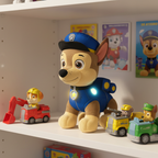 PAW Patrol Room Patrol Chase Interactive Plush Toy (12-inch) — Chase plush in blue police uniform with light-up badges on a bright white playroom shelf alongside other PAW Patrol toys with warm ambient lighting — cheerful gift-ready lifestyle scene