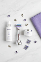 Professional flat lay of luxury women's shaving accessories and skincare products on white marble with platinum and purple accents