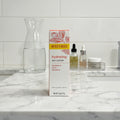 Burt's Bees Hydrating Day Lotion box on bathroom marble vanity alongside clear glass carafe of water and organized acrylic skincare tray