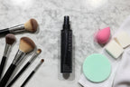 Close-up of beauty tool maintenance station with makeup brushes and dark spray bottle on white marble