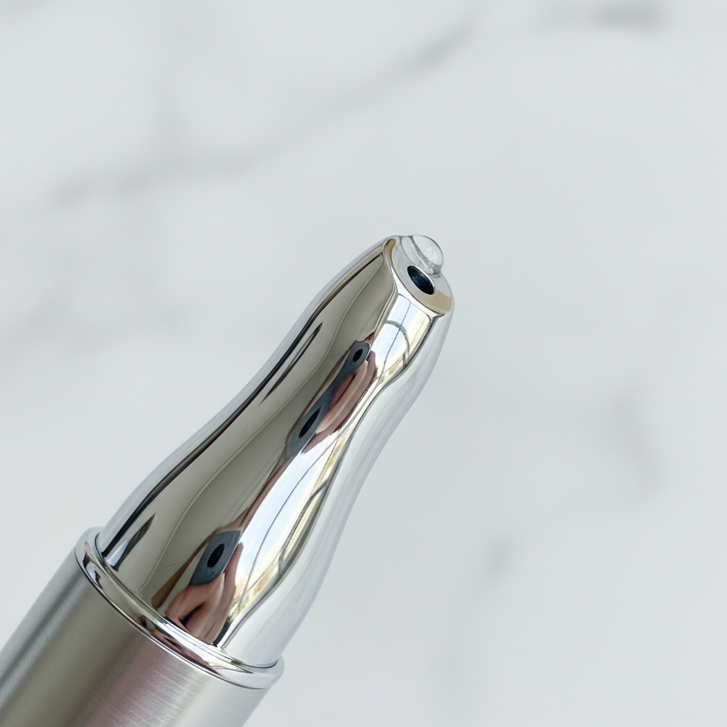 Extreme close-up macro of smooth metallic cooling applicator tip of luxury lip treatment pen on white marble
