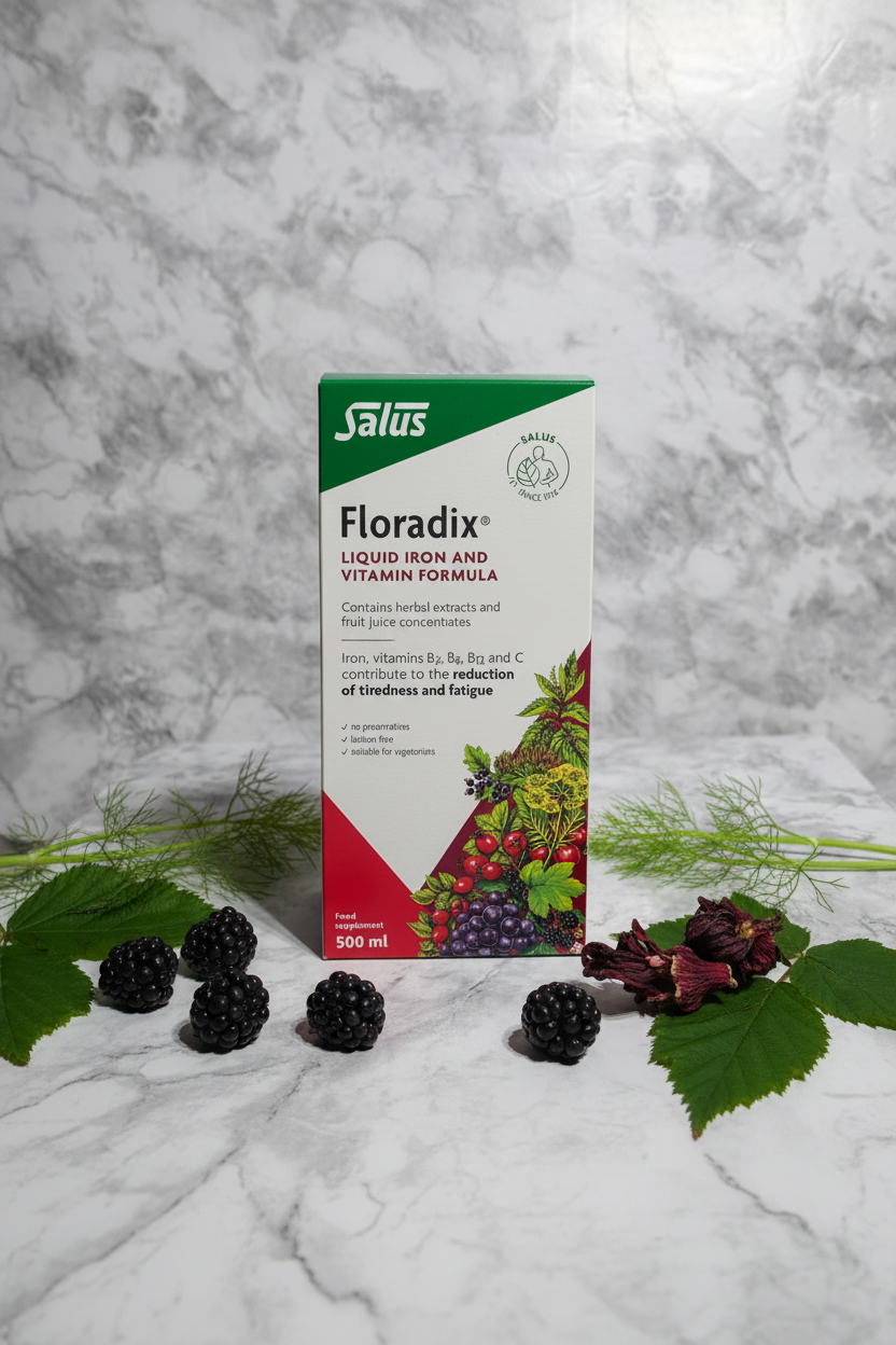 Salus Floradix Iron and Herbs Liquid Formula 500ml retail box on white marble with green and red botanical props, blackberries, fennel fronds, and hibiscus flowers, minimalist studio photography – More4less Outlet