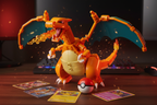 MEGA Pokémon Charizard building set fully assembled with wings spread wide in attack stance on gaming desk with Pokémon cards and dramatic fire lighting
